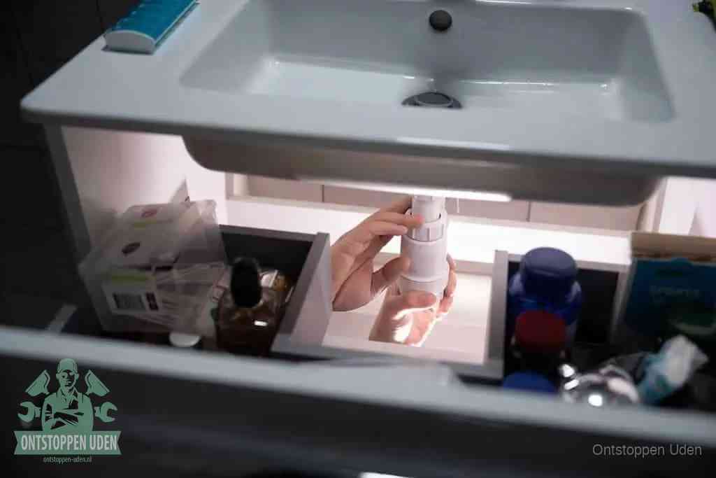 Een pompfles met zeep boven een wastafel, de heet water en afwasmiddel-methode om een vetprop in de afvoer los te maken in Uden