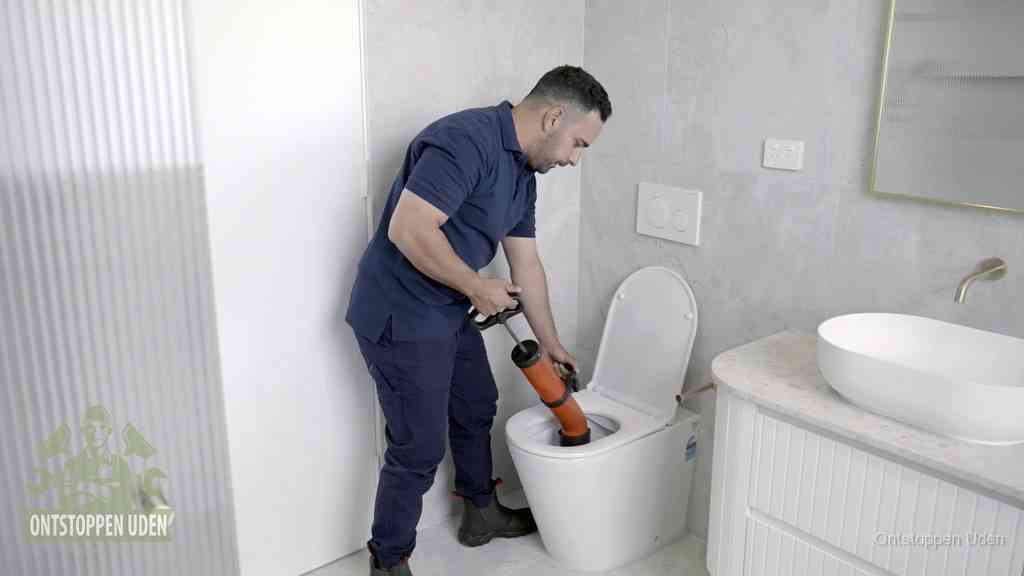 Een monteur buigt over een wandcloset en duwt met de hand een persluchtontstopper in de toiletpot om de verstopping handmatig los te maken in Uden