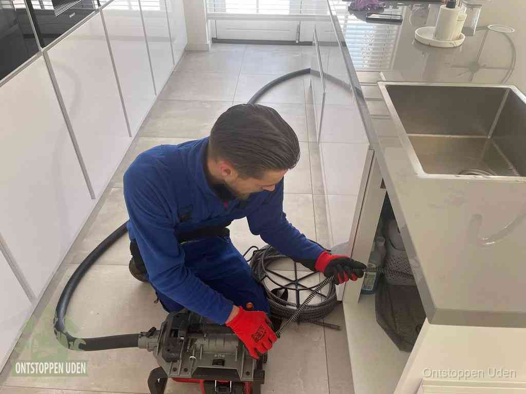 Een monteur ontstopt de keukenafvoer onder de spoelbak met een elektrische veermachine in Uden