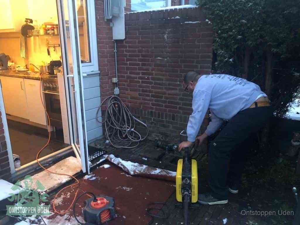 Een monteur werkt buiten bij een open riool-/grondput met een elektrische ontstoppingsmachine om een verborgen afvoerprobleem op te sporen in Uden