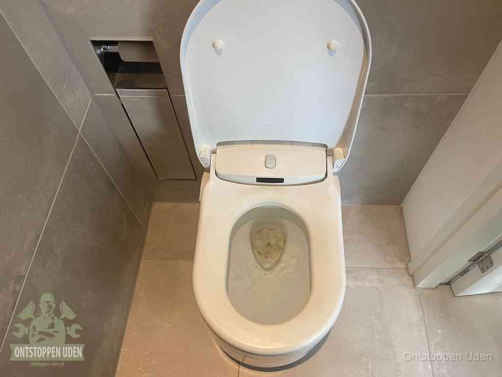 Een wit hangtoilet waarin een prop wc-papier op het water blijft drijven, een duidelijk signaal van een verstopte wc in Uden