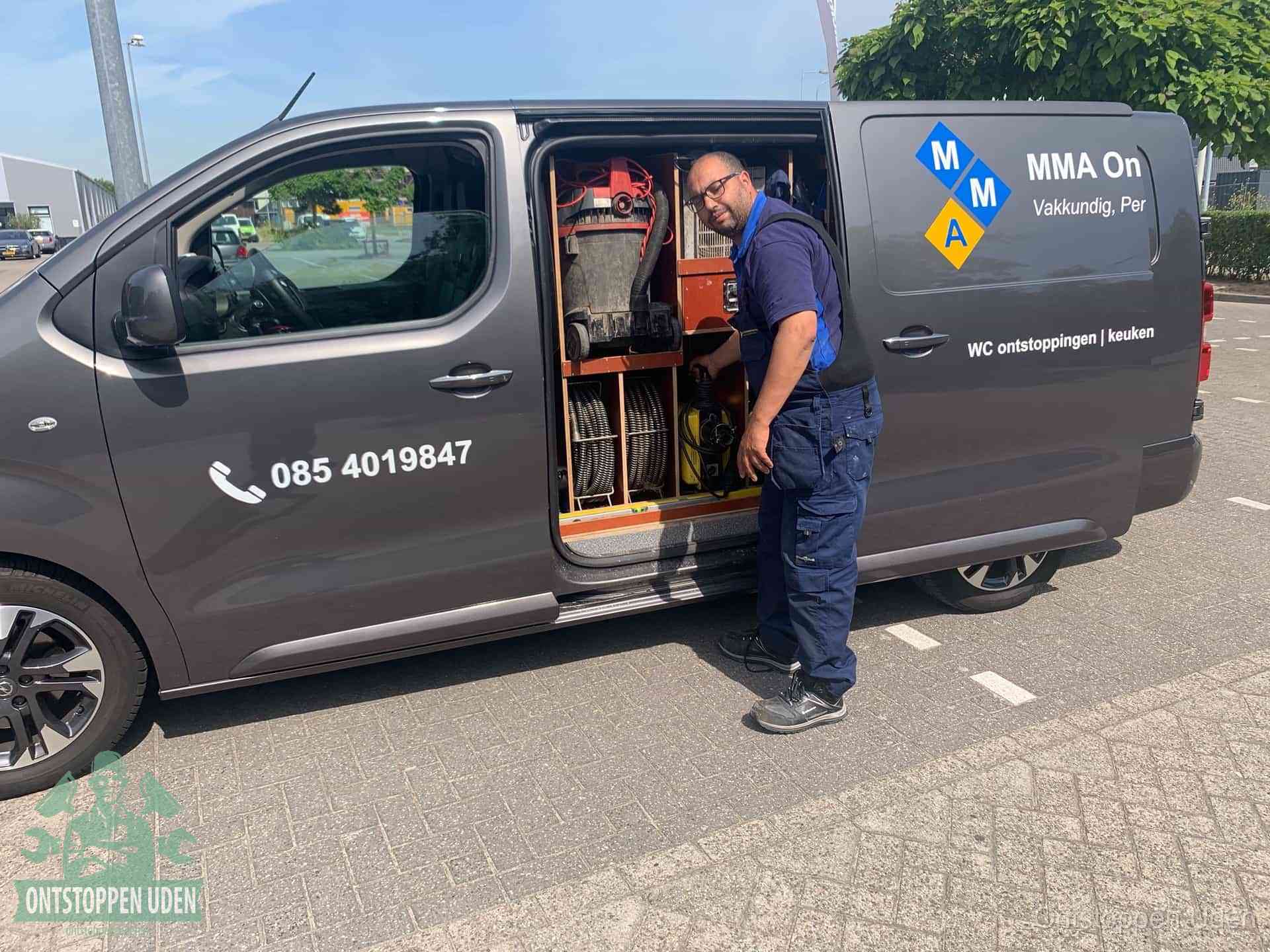 Een monteur bij de open schuifdeur van zijn bedrijfsbus op een parkeerplaats, klaar om de oorzaak van terugkerende afvoerverstoppingen aan te pakken in Uden