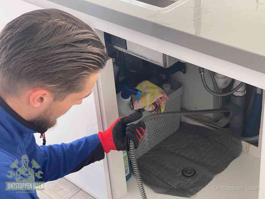 Een monteur voert een flexibele ontstoppingsveer in de afvoer om een verstopping voorbij de bocht van het toilet te bereiken in Uden