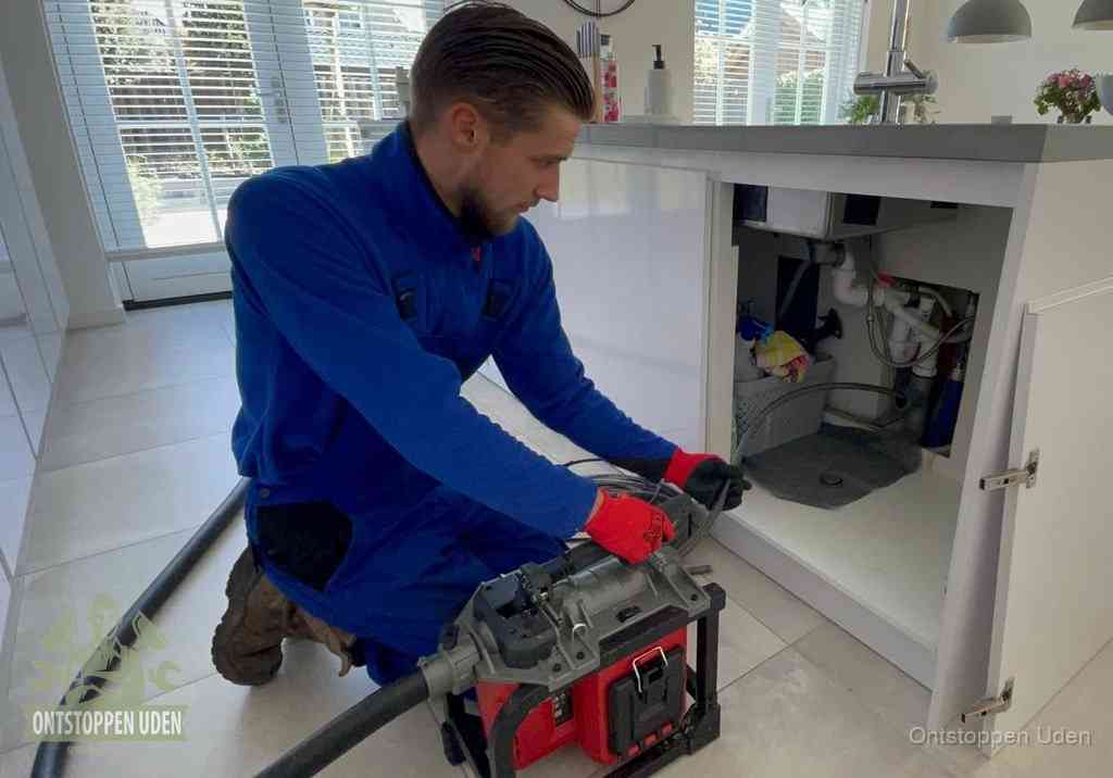 Een monteur voert een professionele elektrische ontstoppingsmachine in de afvoer onder de spoelbak tijdens het gootsteen ontstoppen in Uden
