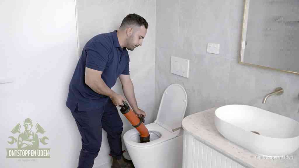 Een man gebruikt een handmatige luchtdruk-ontstopper in een modern betegeld toilet om zelf de wc te ontstoppen in Uden